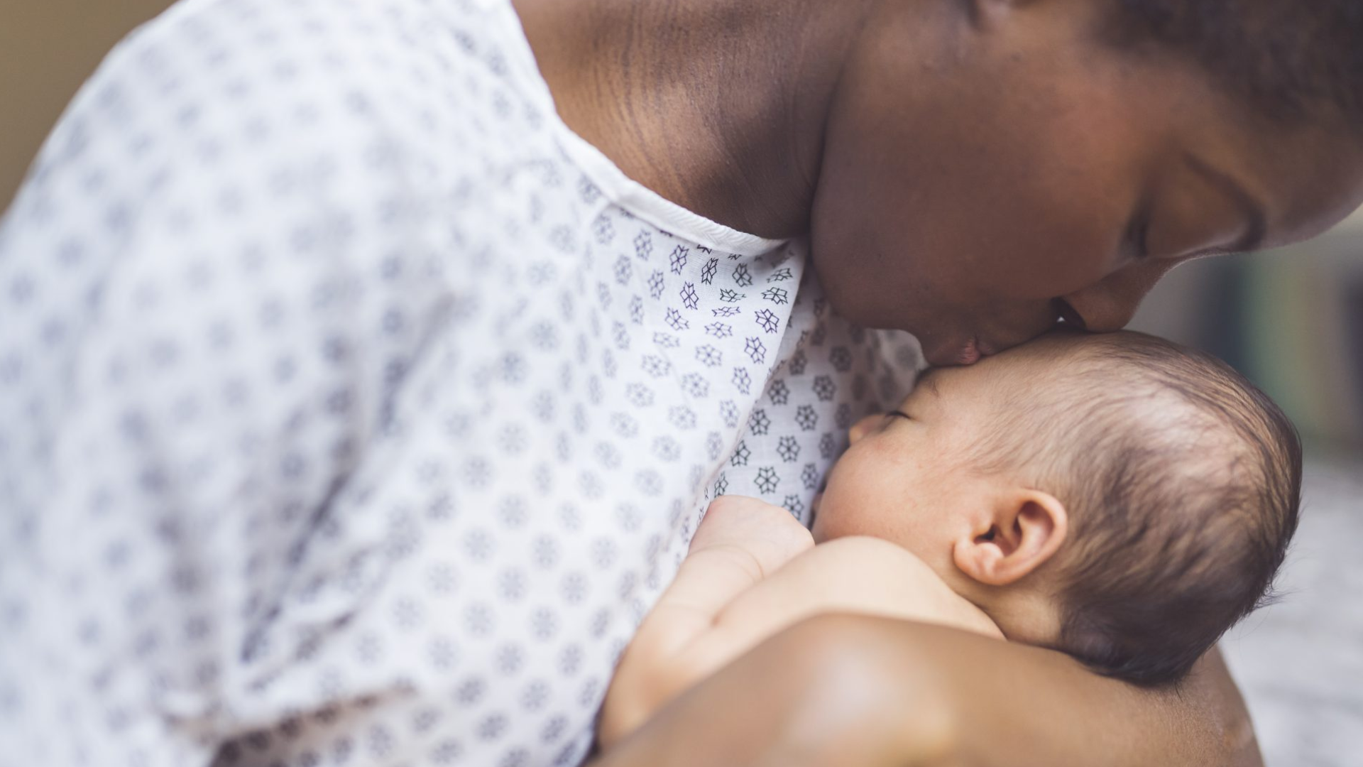 woman wearing hospital gown kissing new born baby